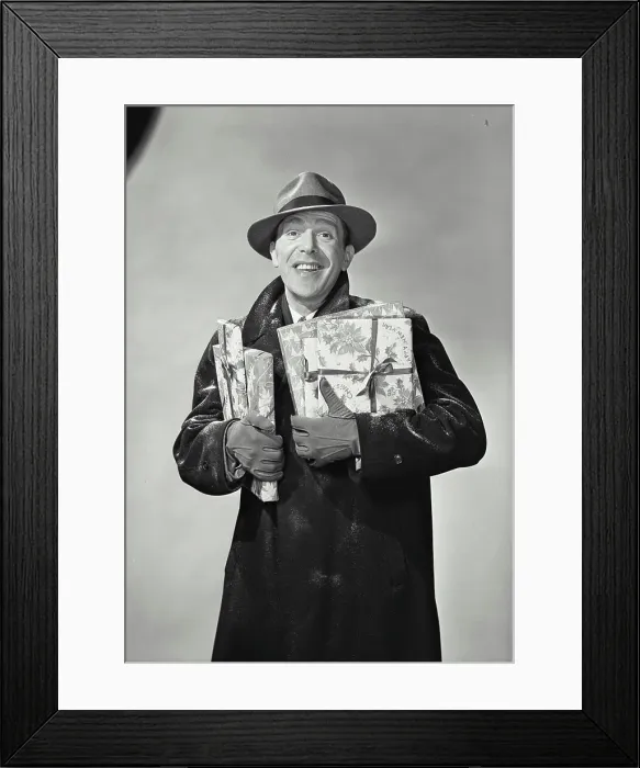 Framed Print : Vintage Photograph. Smiling man wearing hat and winter coat dusted with snow holding wrapped holiday presents