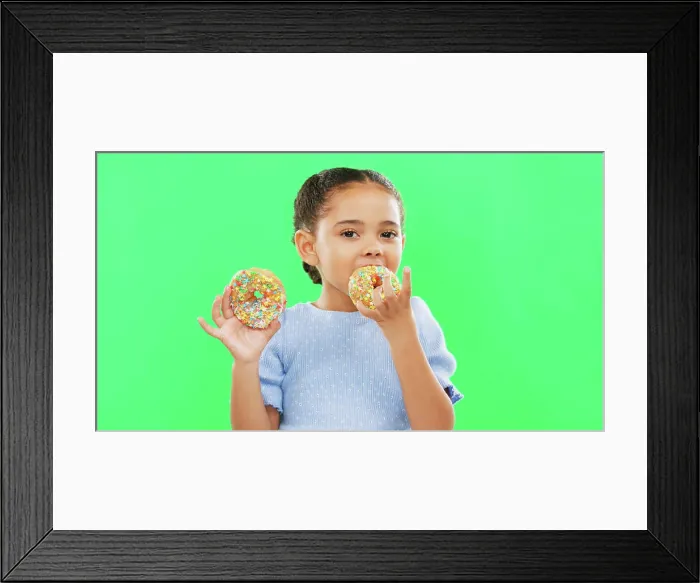 Framed Print : Candy, smile and child eating donuts on green background with cake for party Framed Print : Candy, smile and child eating donuts on green background with cake for party