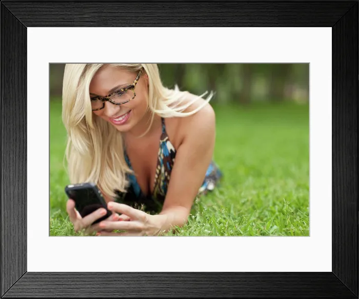 Framed Print : Blonde girl lying on lawn at park and texting