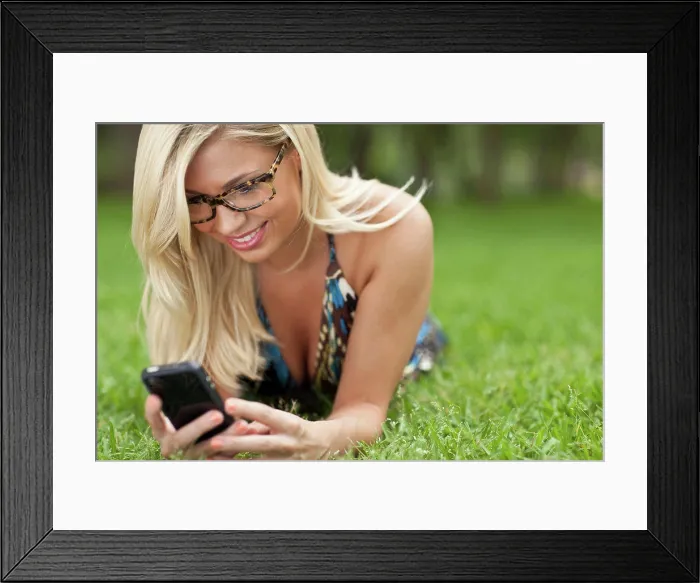 Framed Print : Blonde girl lying on lawn at park and texting Framed Print : Blonde girl lying on lawn at park and texting