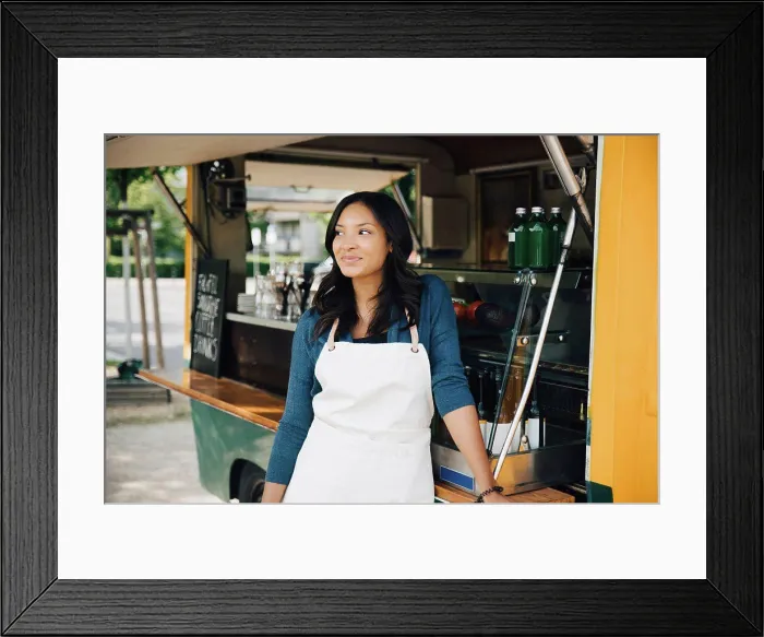 Framed Print : Smiling female owner looking away while standing against food truck