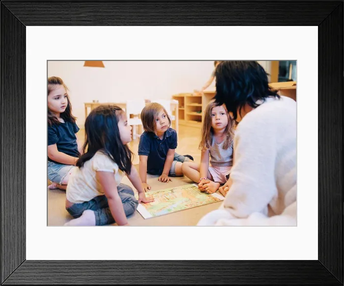 Framed Print : Female teacher telling story to students sitting in classroom at child care Framed Print : Female teacher telling story to students sitting in classroom at child care