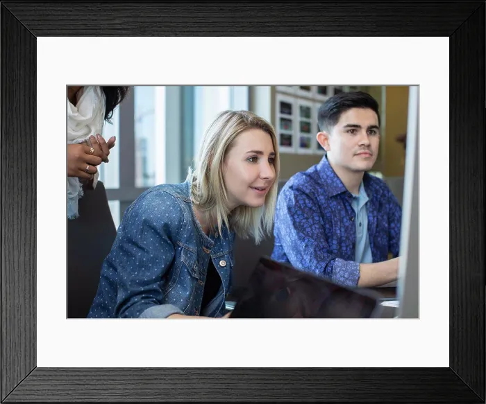 Framed Print : Young woman using computer in office, showing co-workers something on her screen