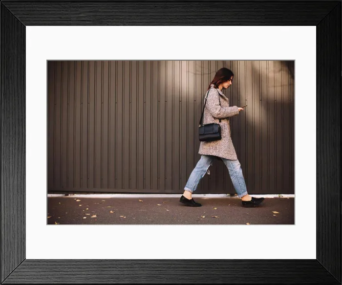 Framed Print : Side view of non-binary woman using smart phone walking against wall Framed Print : Side view of non-binary woman using smart phone walking against wall
