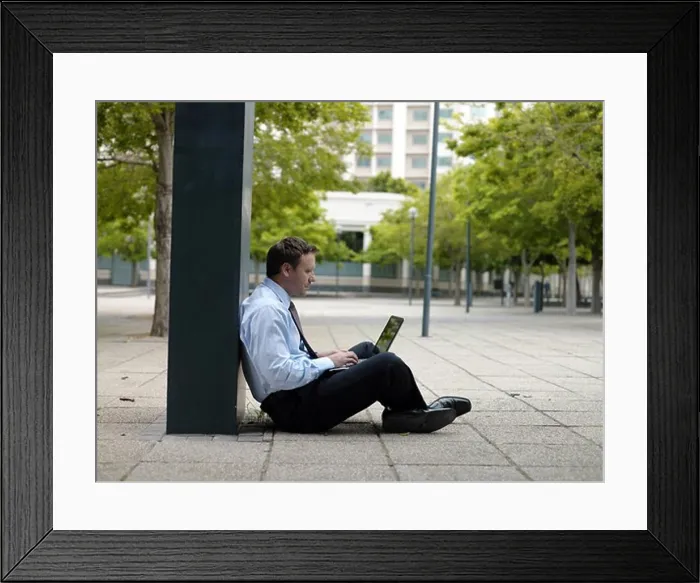 Framed Print : Side profile of businessman sitting at roadside and using laptop Framed Print : Side profile of businessman sitting at roadside and using laptop