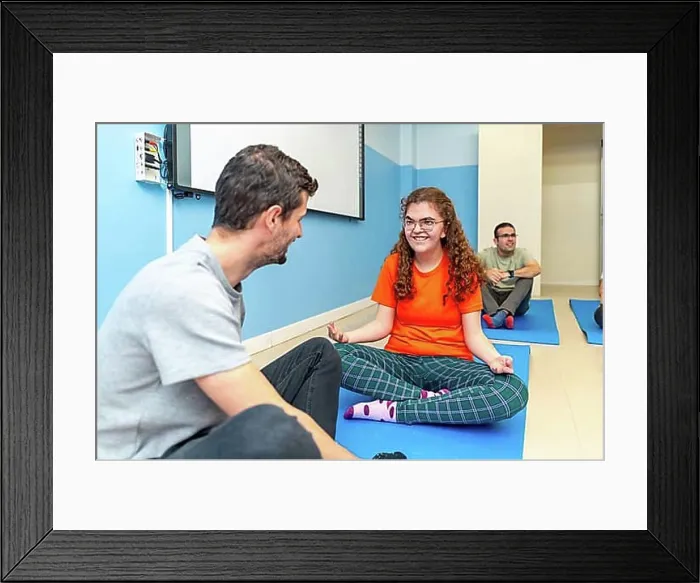 Framed Print : Yoga instructor and disabled woman talking while practicing yoga sitting on a mat with other people
