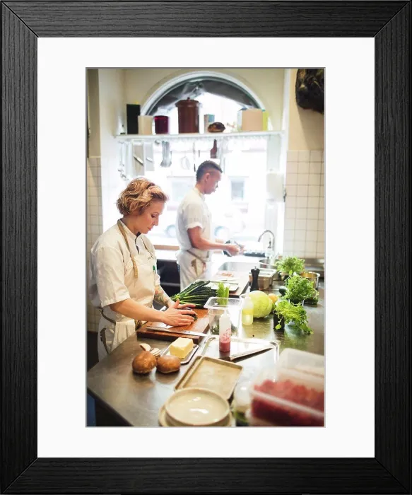 Framed Print : Female chef is cutting vegetables on board by colleague working at counter in restaurant kitchen Framed Print : Female chef is cutting vegetables on board by colleague working at counter in restaurant kitchen