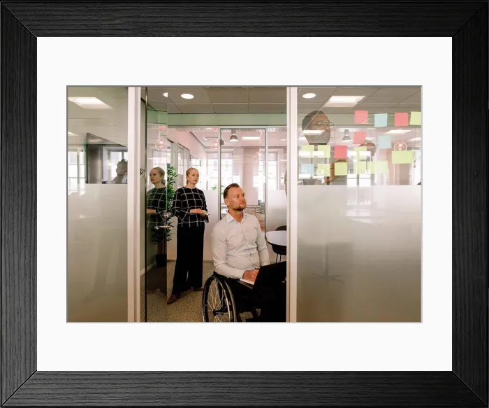 Framed Print : Colleagues looking at businessman sticking adhesive notes on glass wall in board room Framed Print : Colleagues looking at businessman sticking adhesive notes on glass wall in board room