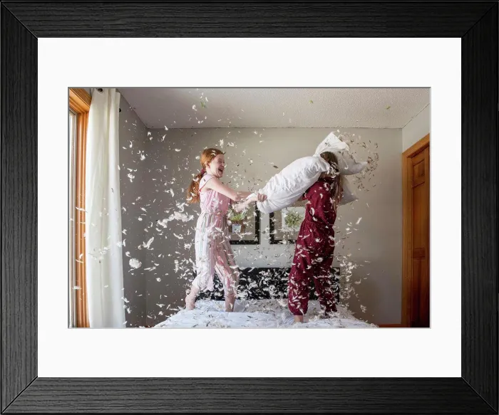 Framed Print : Two happy young girls having a feather pillow fight on the bed Framed Print : Two happy young girls having a feather pillow fight on the bed