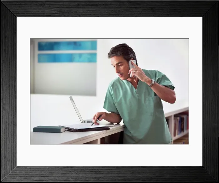Framed Print : Hispanic Male doctor in his home practicing Telemedicine, talking on cell phone and taking notes Framed Print : Hispanic Male doctor in his home practicing Telemedicine, talking on cell phone and taking notes