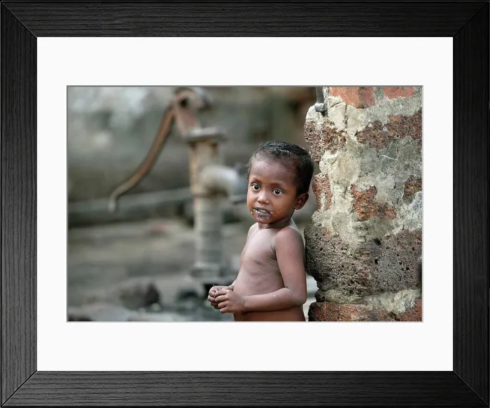 Framed Print : A naked child standing against a wall with a water hand pump in the background; Gopinathpur Village, India Framed Print : A naked child standing against a wall with a water hand pump in the background; Gopinathpur Village, India