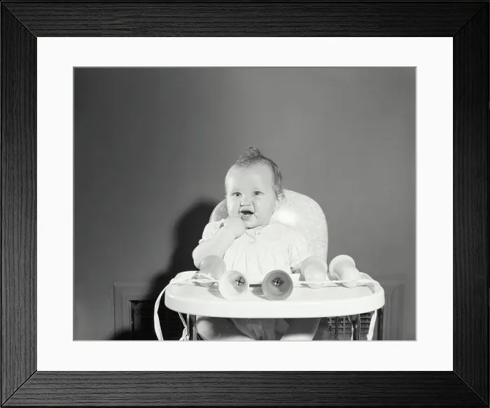 Framed Print : Baby girl sitting in a high chair with her finger in her mouth Framed Print : Baby girl sitting in a high chair with her finger in her mouth