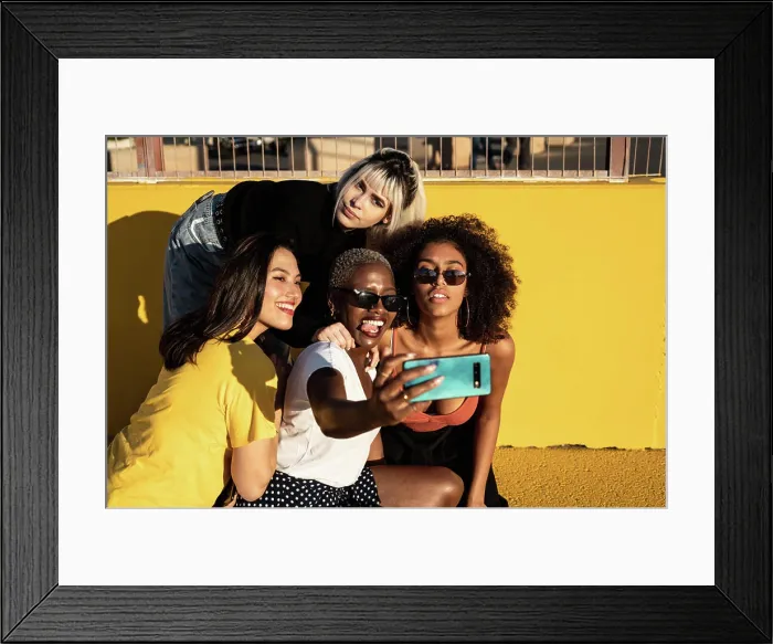 Framed Print : Cheerful young diverse female friends taking selfie on smartphone in street