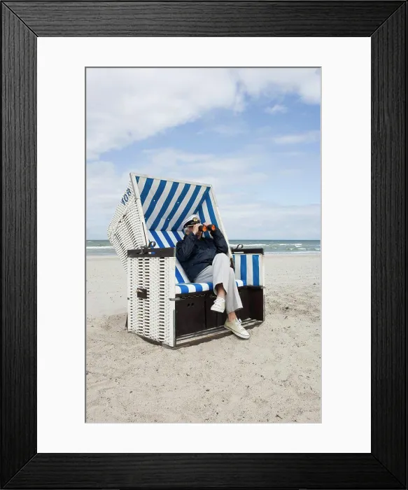 Framed Print : A senior man sitting in a hooded beach chair looking through binoculars Framed Print : A senior man sitting in a hooded beach chair looking through binoculars