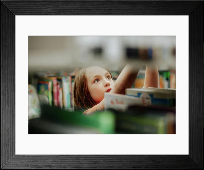 Framed Print : Young girl reaching for library book on shelf Framed Print : Young girl reaching for library book on shelf