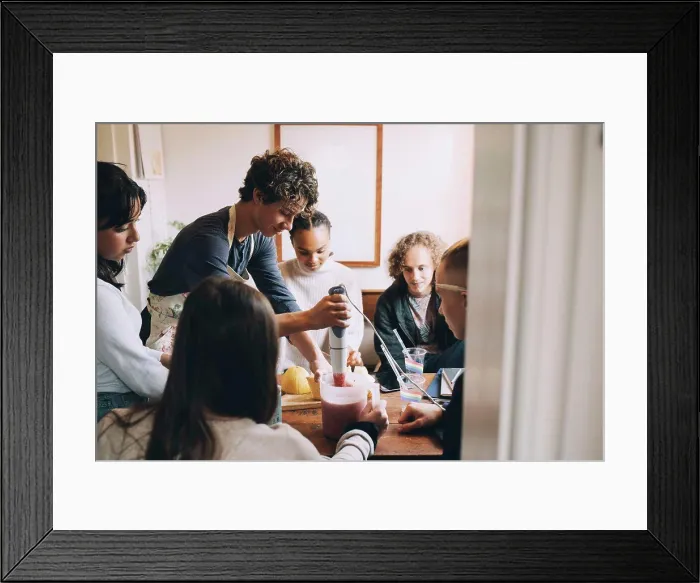 Framed Print : Friends looking at teenage boy preparing smoothie at dining table in room