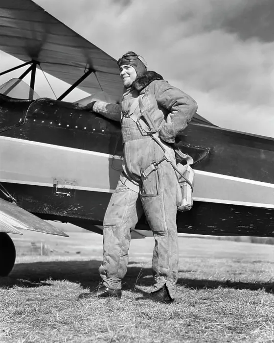 Framed Print : 1940s PORTRAIT SMILING MAN AVIATOR PILOT STANDING BY BIPLANE WEARING CANVAS FLYING SUIT HELMET GOGGLES AND PARACHUTE