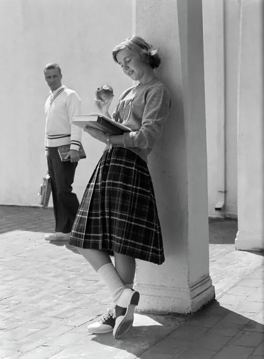 Framed Print : 1950S 1960S Teen School Girl Plaid Skirt Leaning Against Column Eating Apple Reading Book As Boy Walks By In Background Framed Print : 1950S 1960S Teen School Girl Plaid Skirt Leaning Against Column Eating Apple Reading Book As Boy Walks By In Background