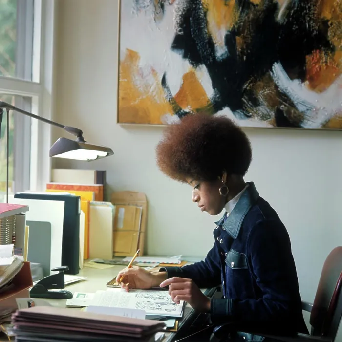 Framed Print : 1960S 1970S African American Woman Student Sitting At Desk Writing Papers By Window Light Afro Hair Style Denim Jacket Framed Print : 1960S 1970S African American Woman Student Sitting At Desk Writing Papers By Window Light Afro Hair Style Denim Jacket