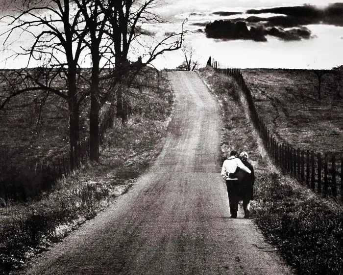 Framed Print : 1960s BACK VIEW MATURE COUPLE ARM IN ARM WALKING DOWN LONELY ROAD BARREN AUTUMN LANDSCAPE WITH OMINOUS CLOUDS ON