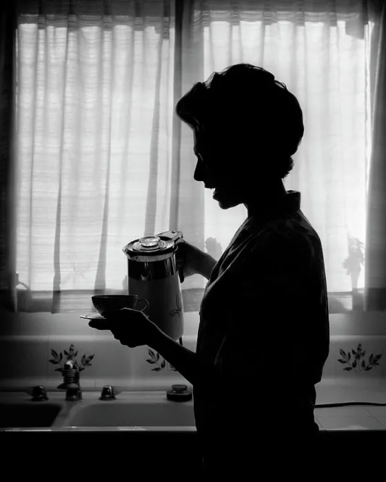 Framed Print : 1970s SILHOUETTED ANONYMOUS WOMAN HOUSEWIFE SPEAKING WHILE POURING FIRST CUP OF MORNING COFFEE IN KITCHEN