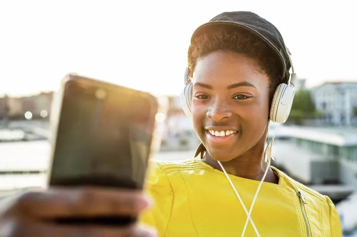 Framed Print : African American woman in stylish bright jacket using mobile phone and listen to music on headphones