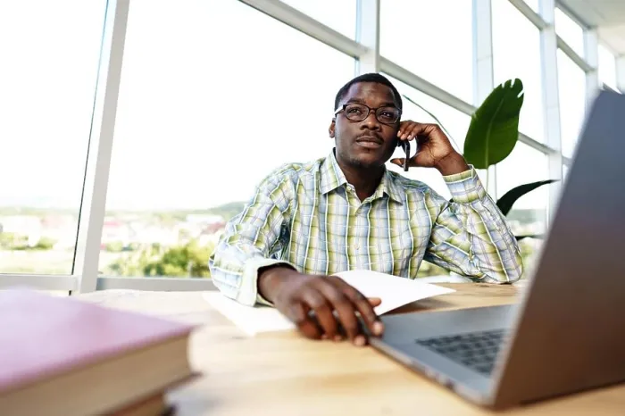 Framed Print : African man entrepreneur talking on cellphone and working on laptop at office Framed Print : African man entrepreneur talking on cellphone and working on laptop at office