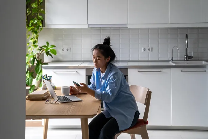 Framed Print : Asian woman sits at the kitchen table with a laptop Framed Print : Asian woman sits at the kitchen table with a laptop