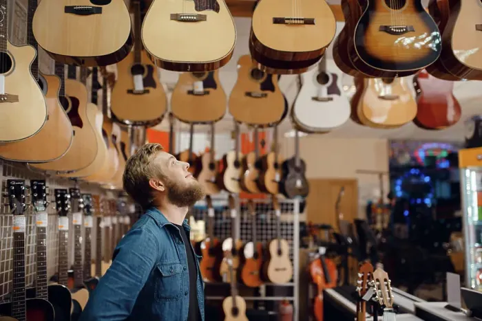 Framed Print : Bearded young guy choosing acoustic guitar in music store Framed Print : Bearded young guy choosing acoustic guitar in music store