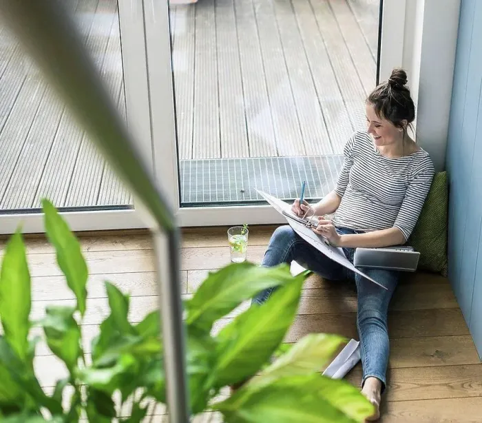 Framed Print : Bird's eye view of smiling woman sitting at the window at home working with laptop and file folder