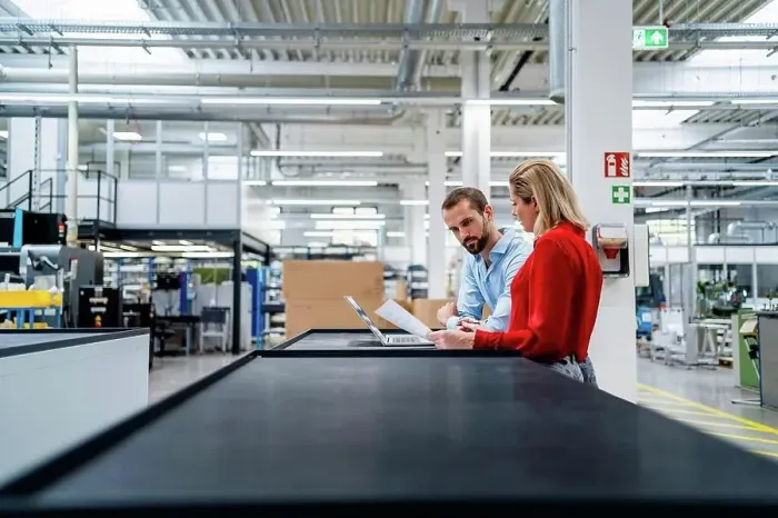 Framed Print : Business colleagues working on laptop at table in factory Framed Print : Business colleagues working on laptop at table in factory