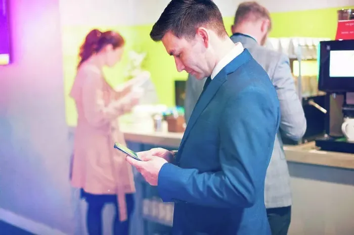 Framed Print : Businessmen and women getting coffee in airport lounge, man in foreground using smartphone Framed Print : Businessmen and women getting coffee in airport lounge, man in foreground using smartphone