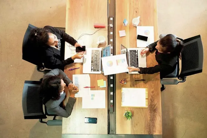 Framed Print : Three businesswomen sitting at desk, using laptop, looking at smartphone, overhead view Framed Print : Three businesswomen sitting at desk, using laptop, looking at smartphone, overhead view