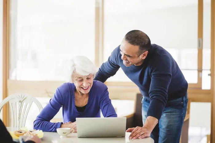 Framed Print : Cheerful mature man standing by mother looking at laptop on table in nursing home Framed Print : Cheerful mature man standing by mother looking at laptop on table in nursing home