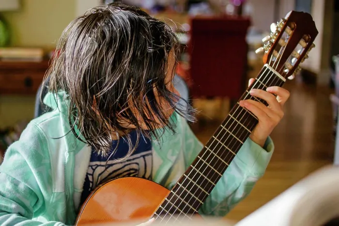 Framed Print : A child with hair hanging in his face practices classical guitar