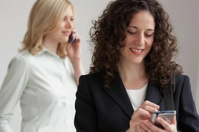 Framed Print : Close-up of a businesswoman using a PDA with another businesswoman talking on a mobile phone Framed Print : Close-up of a businesswoman using a PDA with another businesswoman talking on a mobile phone