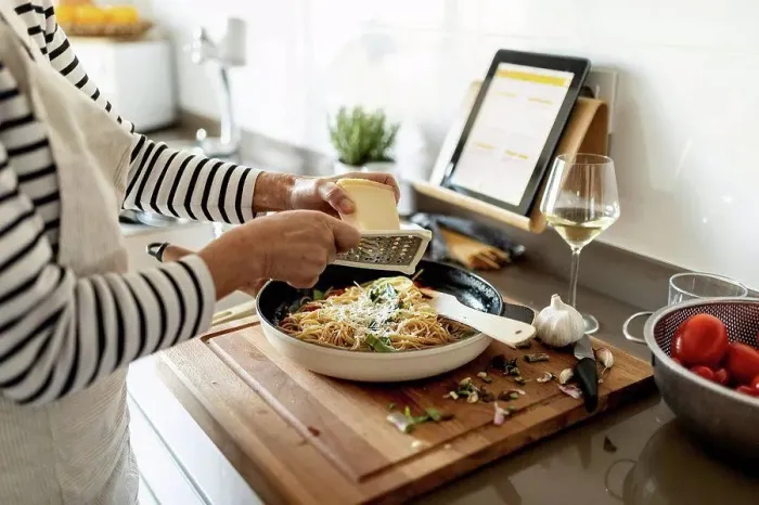 Framed Print : Close-up of woman with tablet cooking pasta dish in kitchen at home Framed Print : Close-up of woman with tablet cooking pasta dish in kitchen at home