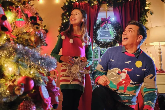 Framed Print : Couple decorating Christmas tree together wearing festive holiday sweaters in colorfully lit living room