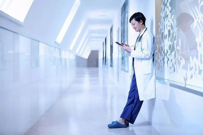 Framed Print : Doctor in hospital corridor leaning against wall using smartphone Framed Print : Doctor in hospital corridor leaning against wall using smartphone