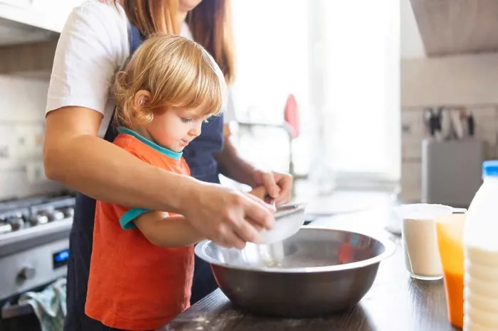 Framed Print : Family in a kitchen. Mother and child sieving flour into a bowl