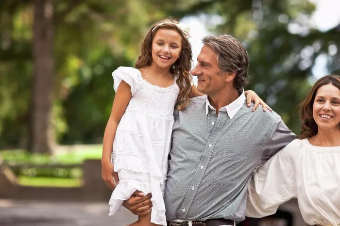 Framed Print : Father holds his daughter in his arms while standing beside his wife