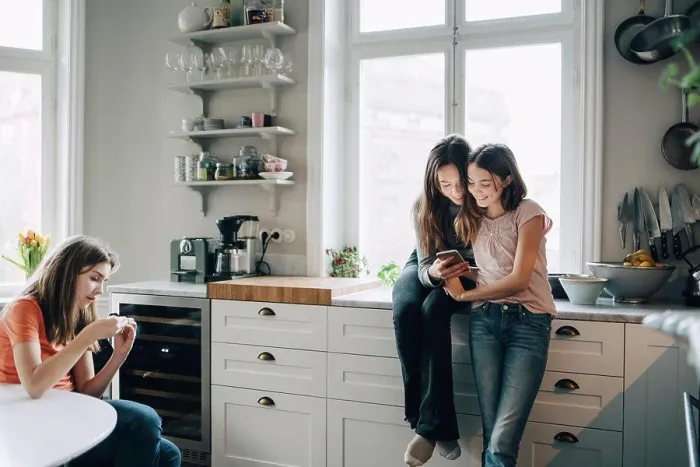 Framed Print : Female friends using mobile phone in kitchen at home Framed Print : Female friends using mobile phone in kitchen at home