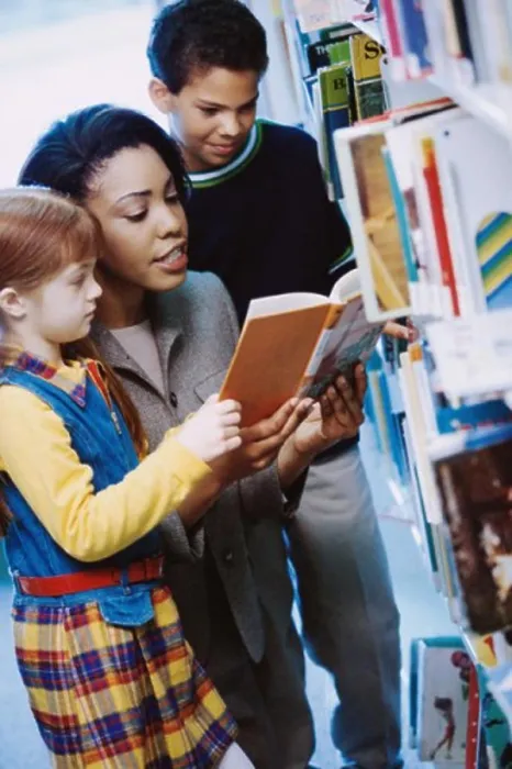 Framed Print : Female teacher reading a book with two students