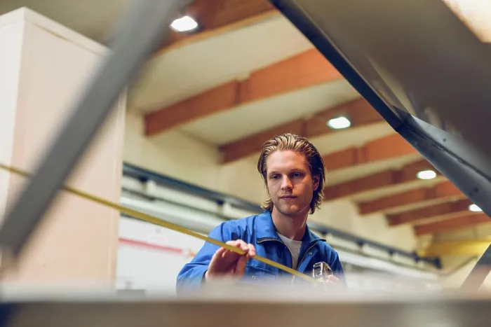 Framed Print : Focused young man using measurement tape to find length in factory Framed Print : Focused young man using measurement tape to find length in factory
