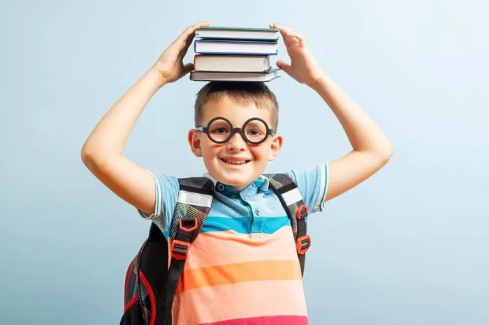 Framed Print : Funny smiling school boy in glasses holds books on his head on blue background Framed Print : Funny smiling school boy in glasses holds books on his head on blue background