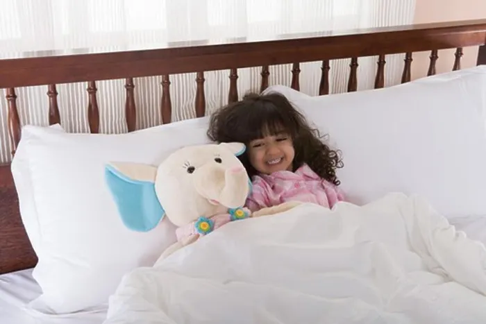 Framed Print : Girl (3-4) lying on bed by toy, smiling Framed Print : Girl (3-4) lying on bed by toy, smiling