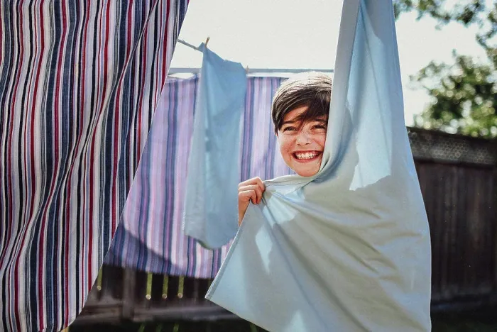 Framed Print : Happy boy hiding behind clothes hanging on a clothesline outside