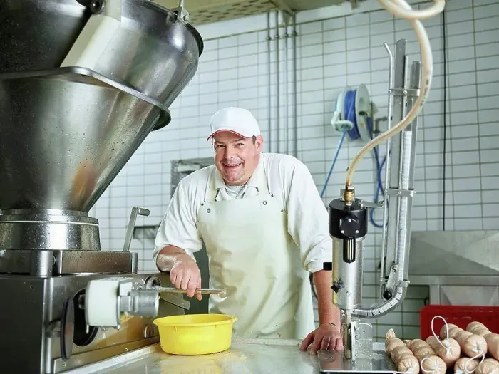 Framed Print : Happy butcher standing by machinery in factory Framed Print : Happy butcher standing by machinery in factory
