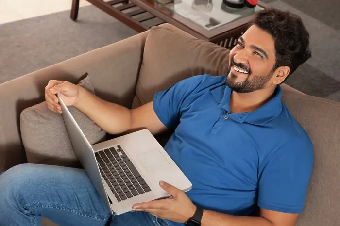 Framed Print : A happy man sitting on couch working on laptop at his home