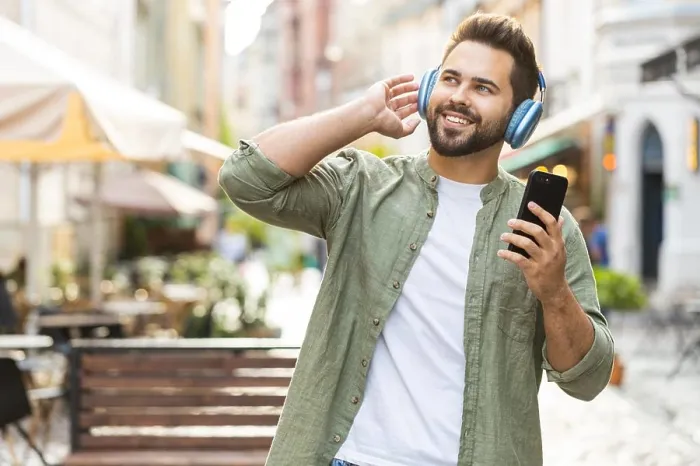 Framed Print : Happy young man in wireless headphones choosing, listening music in smartphone dancing outdoors Framed Print : Happy young man in wireless headphones choosing, listening music in smartphone dancing outdoors